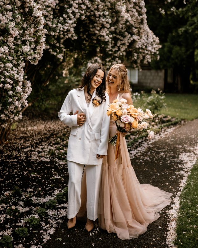Honey yellow wedding inspiration with two brides in a peach wedding dress and white bridal suit
