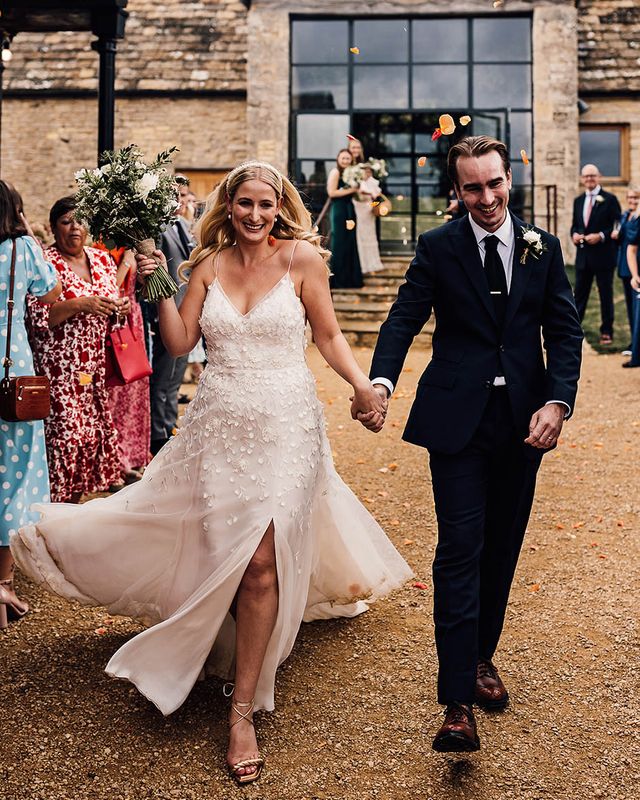 Bride in an Alexandra Grecco Lana wedding dress walking with the groom in a dark blue suit.
