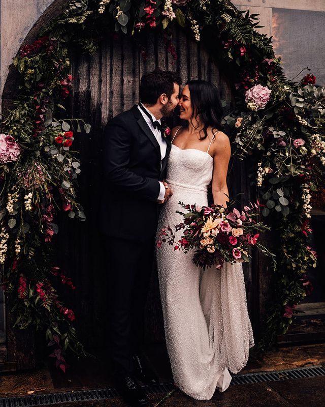 Bride in a beaded sparkle wedding dress with the groom in black tie surrounded by pink flowers.