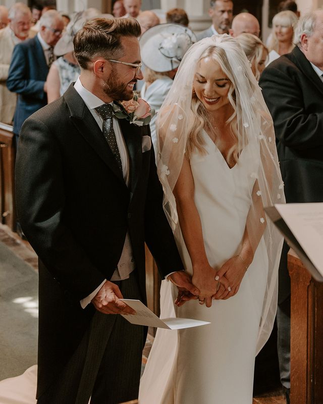 Bride wearing a flower applique veil standing with the groom for their church ceremony.