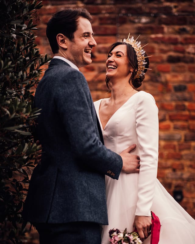 Bride in gold and crystal bride crown in layered wedding dress with groom in navy suit.
