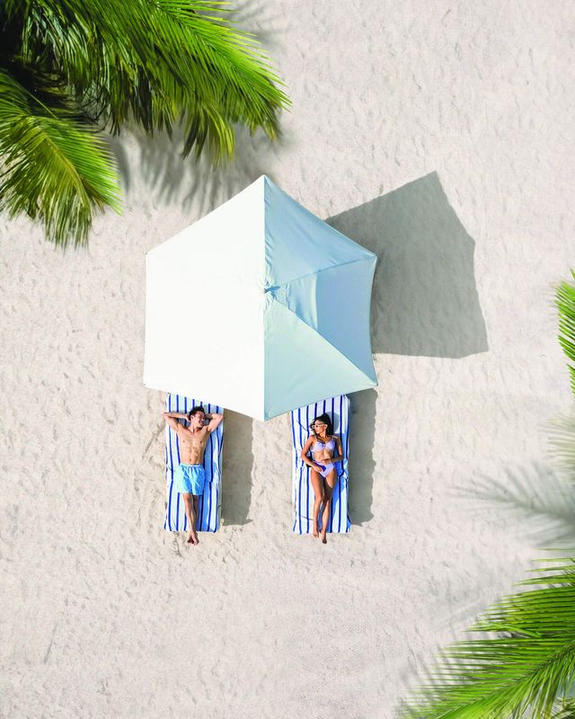Couple relaxing on a white-sand beach under a parasol at a Sandals Resorts adults-only all-inclusive Caribbean honeymoon destination