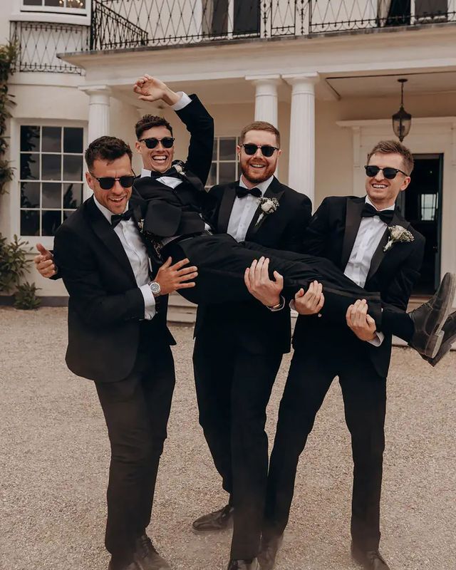 Groomsmen lifting groom in black tie tuxedos