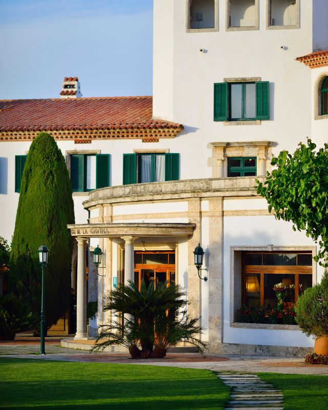 White Mediterranean-style exterior of Hostal de La Gavina in Costa Brava, Spain, featuring green shutters, gardens and elegant architecture at sunset for the perfect honeymoon hotel in Spain 