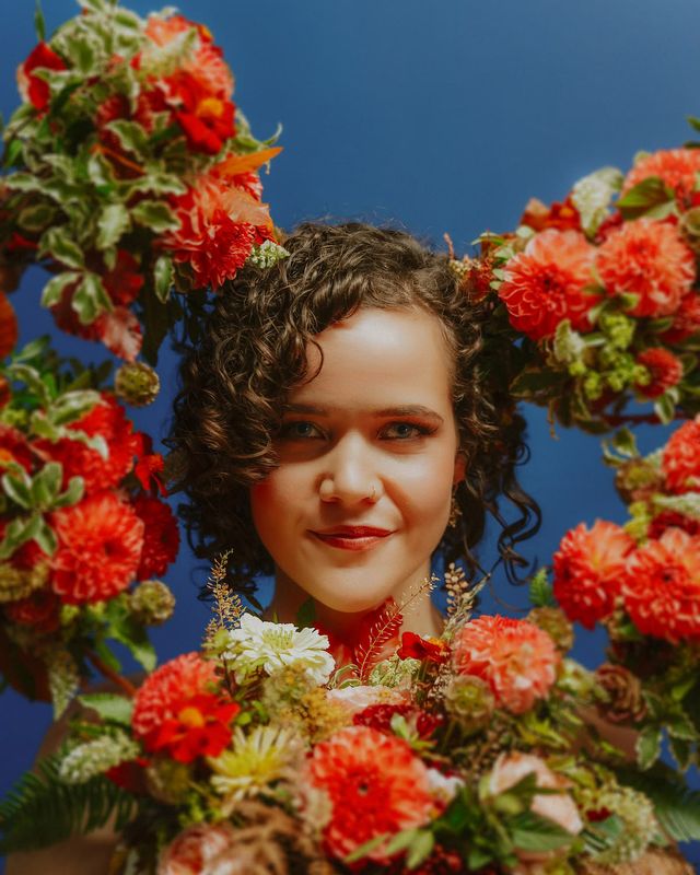 Bride with glowing skin and bridesmaids holding coral dahlia wedding bouquets around her face