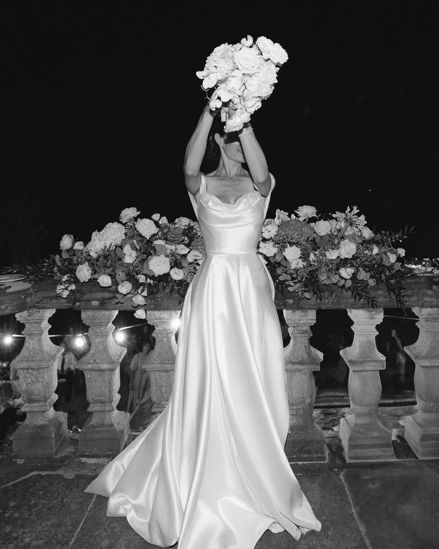 Black and white photo of a bride in a floor-length wedding dress holding a bouquet raised in the air.