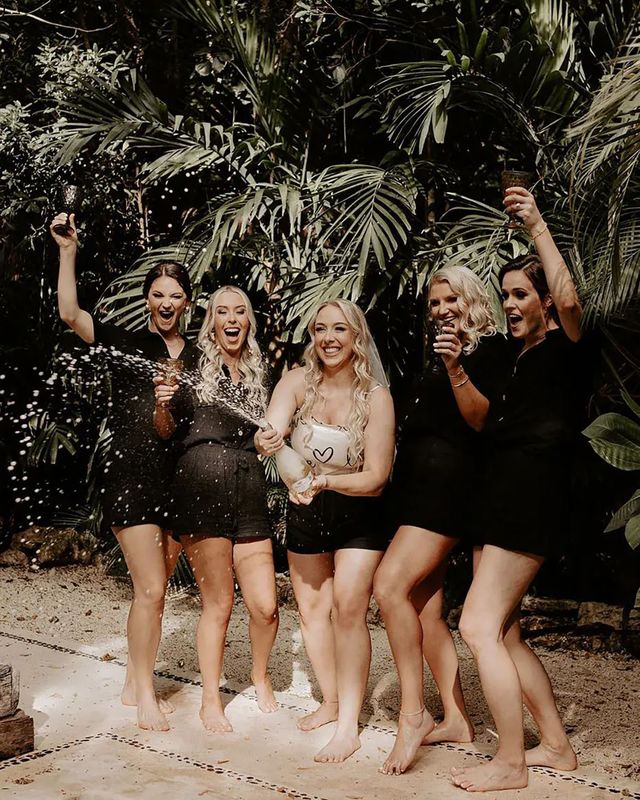 Bridal party wearing matching black pjs spraying champagne for hen do