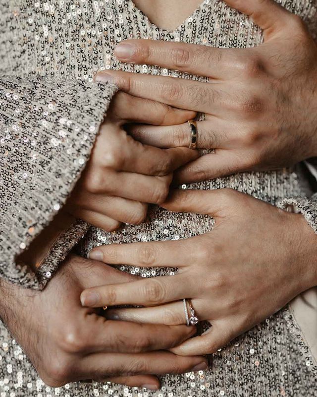 Couple holding hands across silver sparkly wedding dress with engagement rings