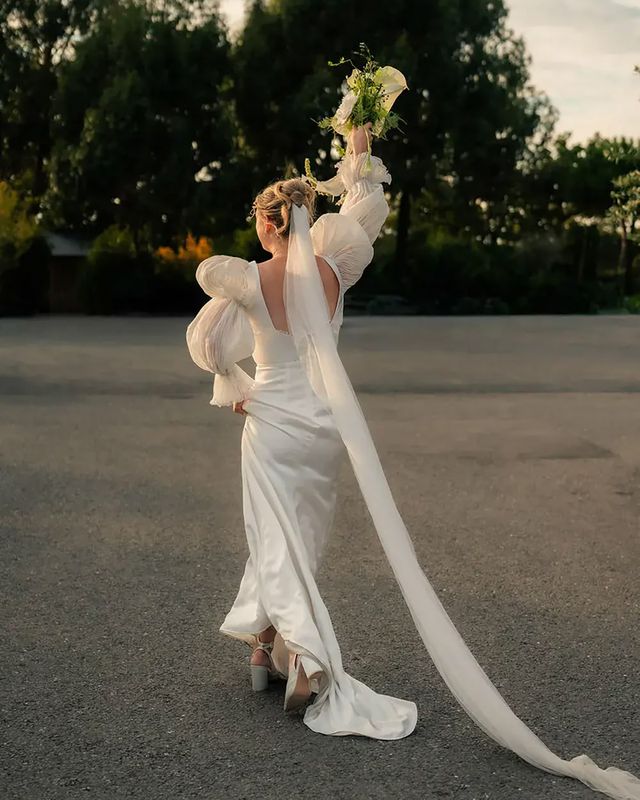 Bride wearing vintage style puff sleeve wedding dress holding bouquet in the air