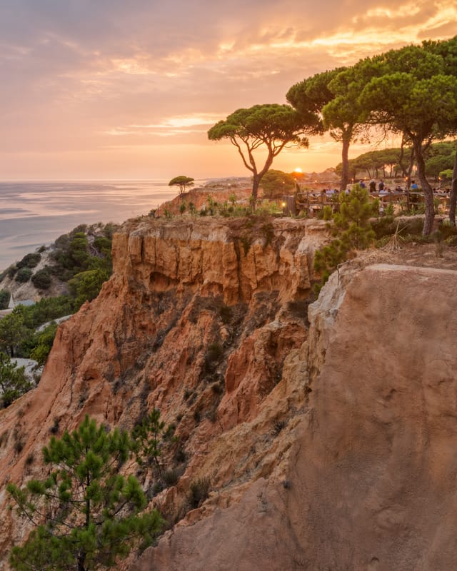 Sunset over the Atlantic Ocean at Pine Cliffs Resort in the Algarve, Portugal, featuring dramatic golden cliffs, pine trees and a scenic clifftop terrace overlooking the coastline.
