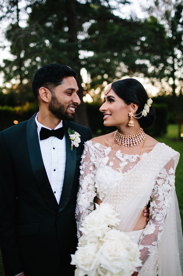 Groom in a black tuxedo and bride in a white sari for multicultural wedding