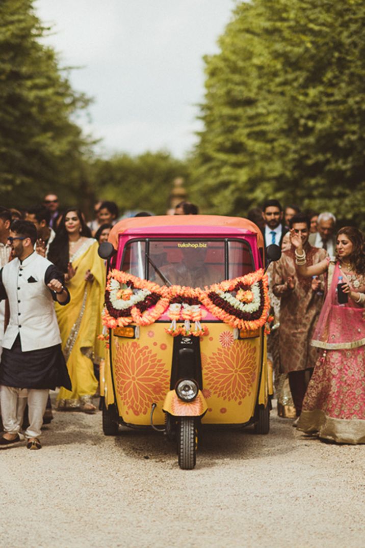 Indian wedding ceremony with orange, yellow and pink Tuk Tuk with colourful floral garland decorations