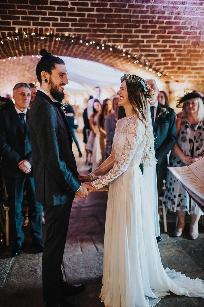 Bride in a lace long sleeve wedding dress and flower crown smiling holding hands with her groom during the civil wedding ceremony