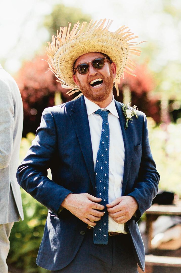 Best man in blue suit with boutonnière, sunglasses and straw hat