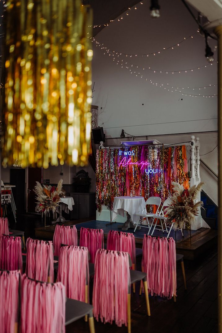 Pink streamers decorated the ceremony chairs for an eclectic wedding with a neon sign and metallic streamer decor 