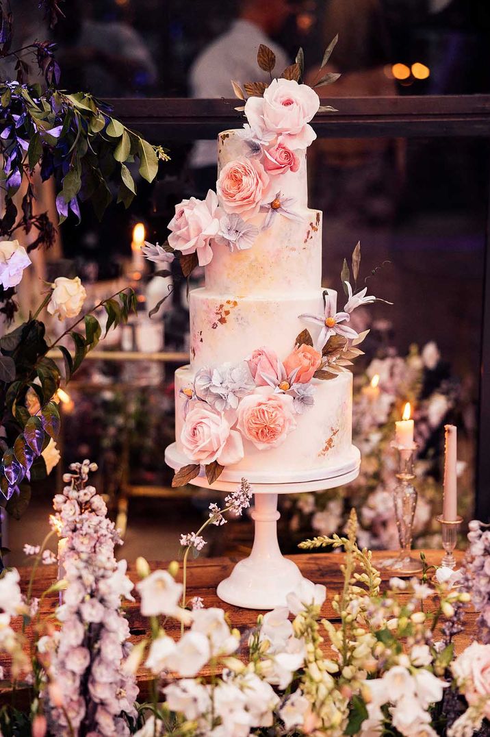 Four tier white iced wedding cake with gold flakes with pink and purple flowers made by Terre Et Lune Cake Design 