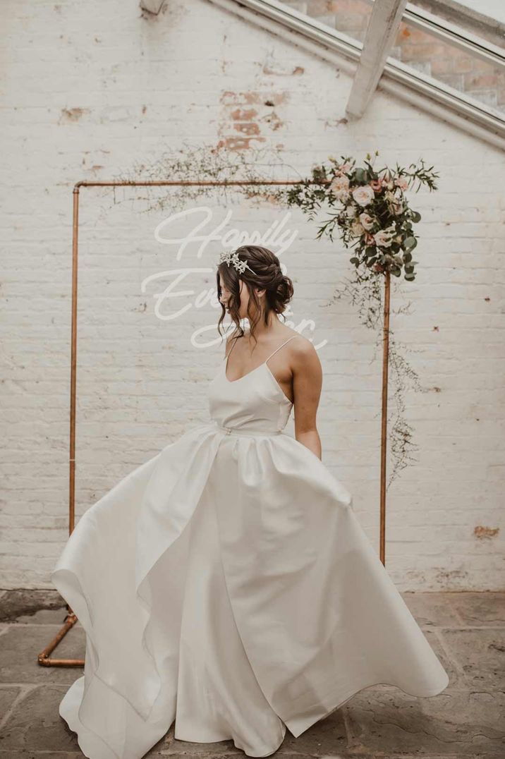 Bride in a princess wedding dress with thin straps in front of neon sign at Garthmyl Hall 