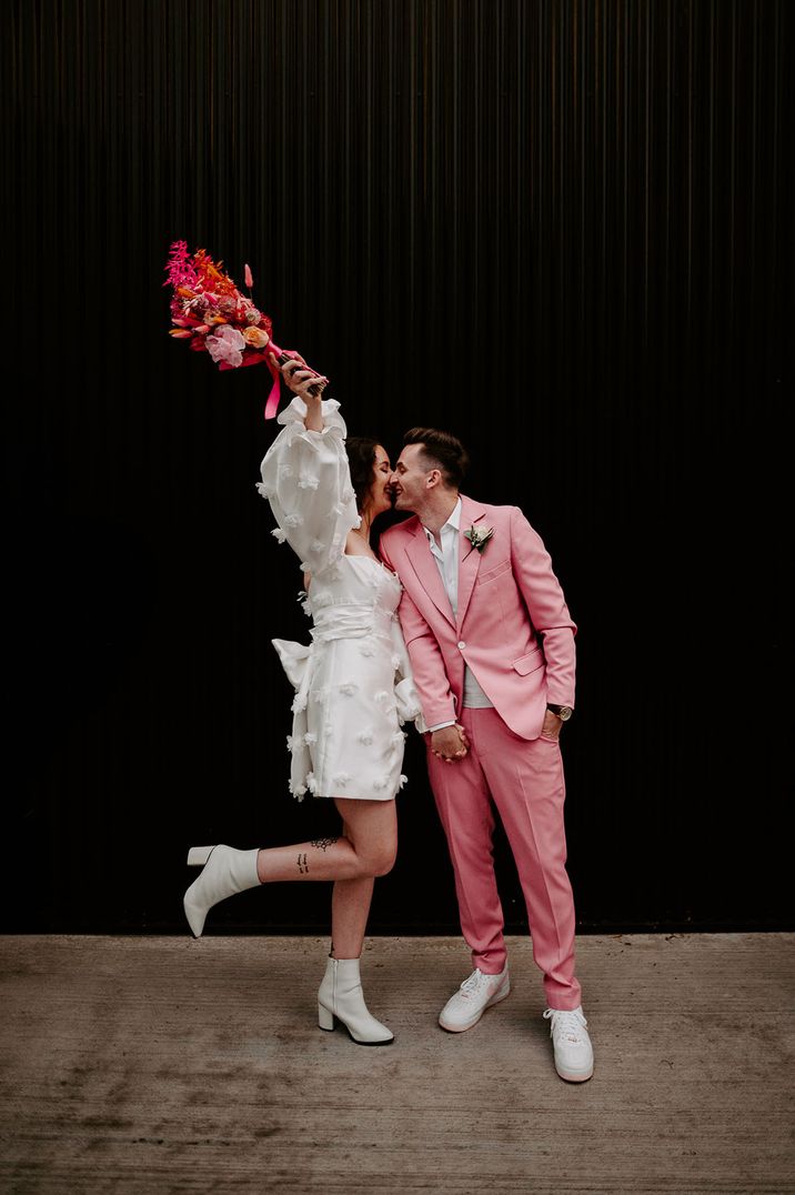 Bride wearing short wedding dress with white boots and pink bouquet 