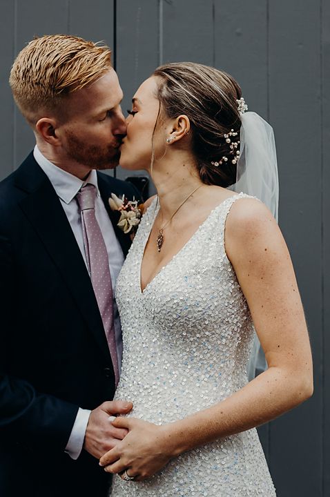 Groom in a dark suit kissing his pregnant bride in a sparkly ASOS wedding dress