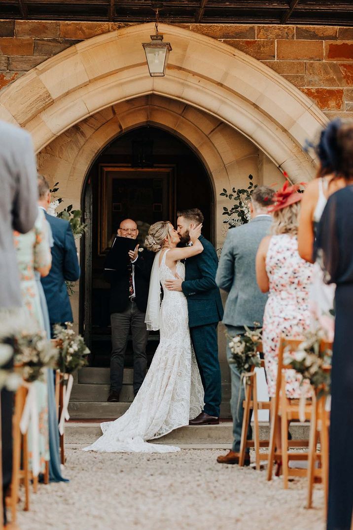 Bride in sleeveless lace detail wedding dress and groom in dark suit kissing at Plas Dinam country house