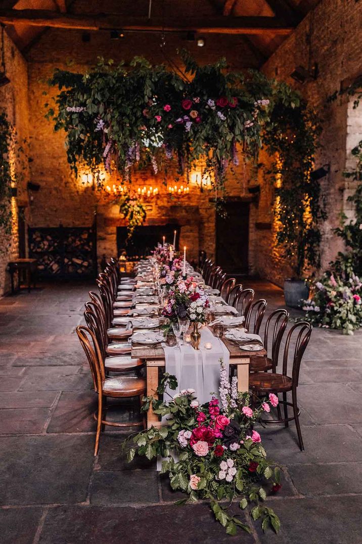 Rustic botanical wedding tablescape at Cripps Barn wedding venue - suspended foliage and garden rose decor, tapered candles, brass and gold vases and light grey sheer table runner 