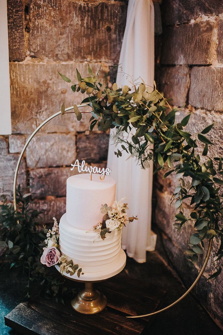 Winter wedding cake with floral decor, an 'always' cake topper and small moongate backdrop 