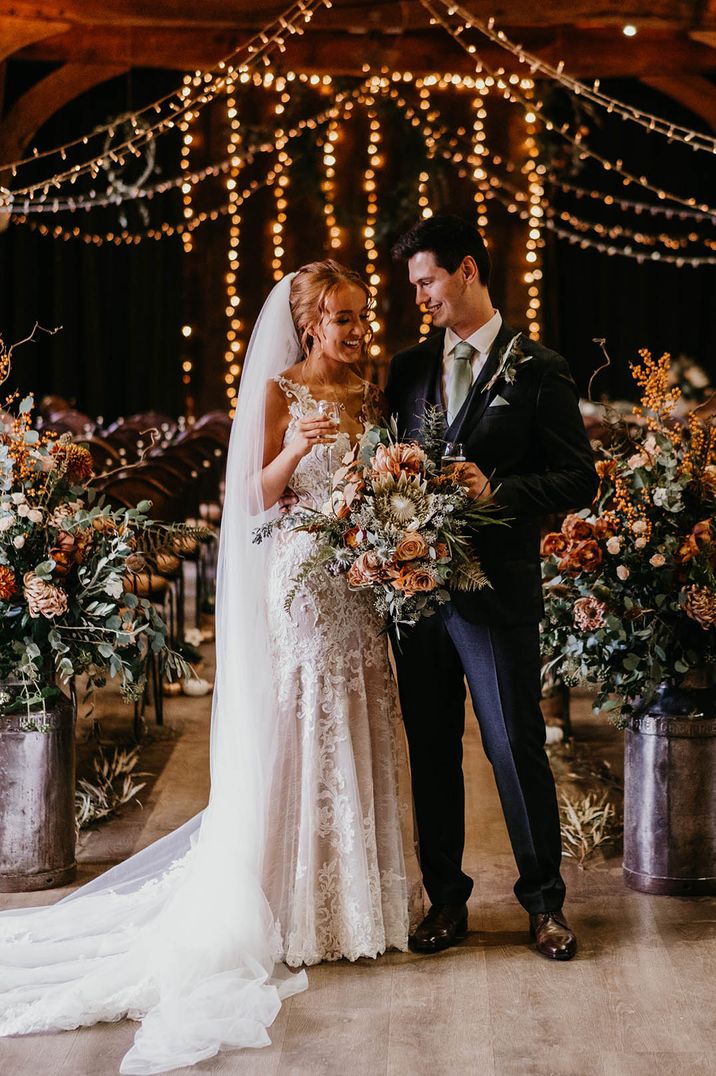 Bride and groom at the fairy lit Tythe Barn wedding venue with an abundance of orange and white flowers 