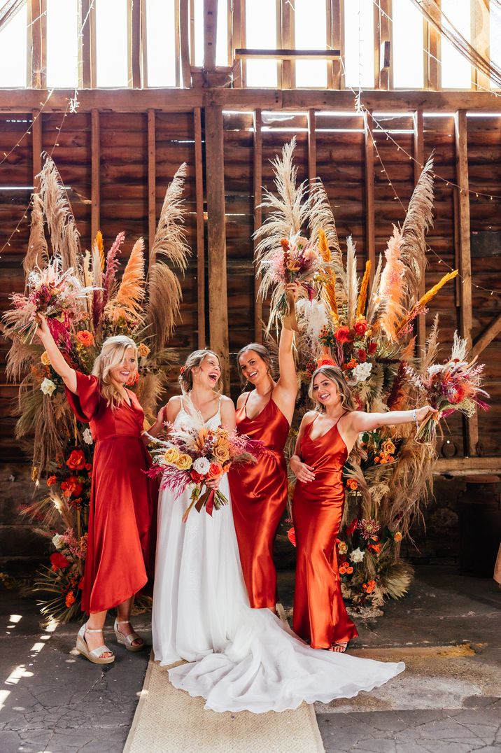 Bride standing with bridesmaids in burnt orange satin bridesmaid dresses from Rewritten Bridesmaids