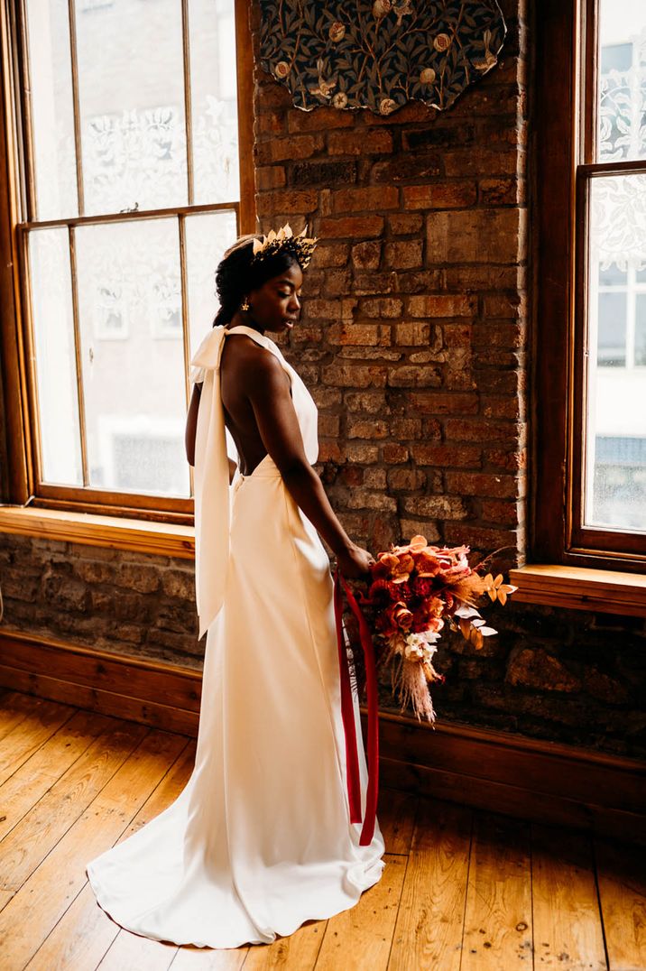 Black bride wearing a halter neck satin slip wedding dress with an open back design 