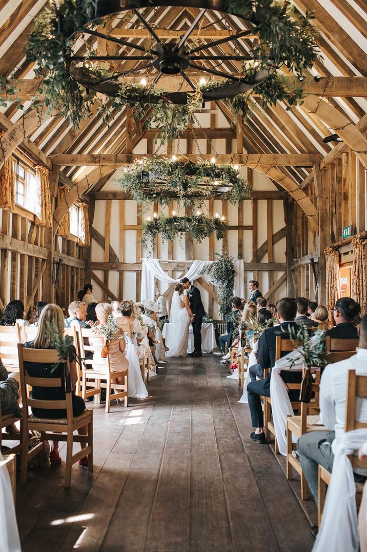 The bride and groom share their first kiss as a married couple with white drapery aisle decorations 