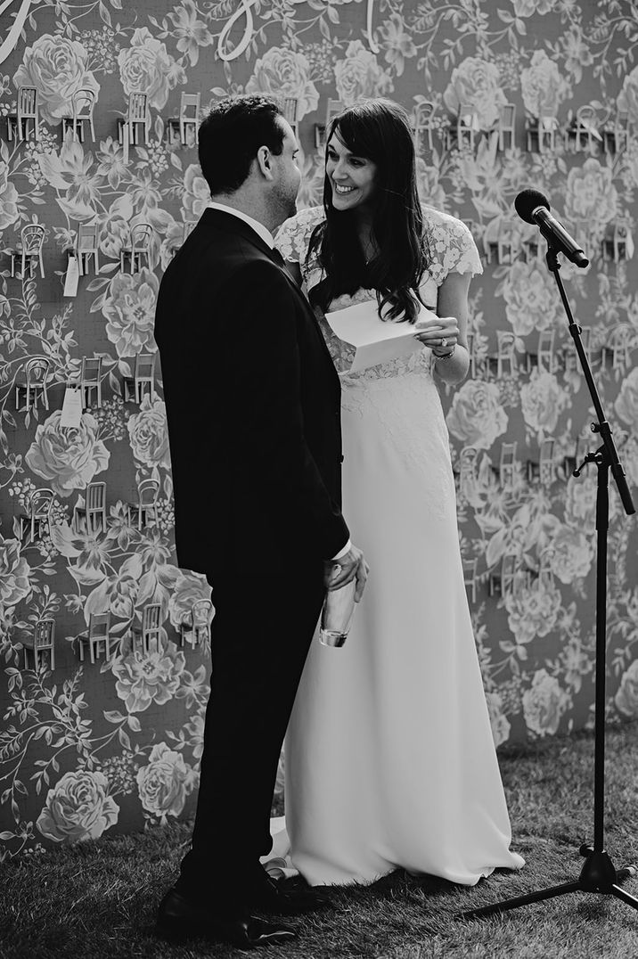 Bride in floral lace short sleeve wedding dress standing with the groom as they deliver their shared wedding speech 