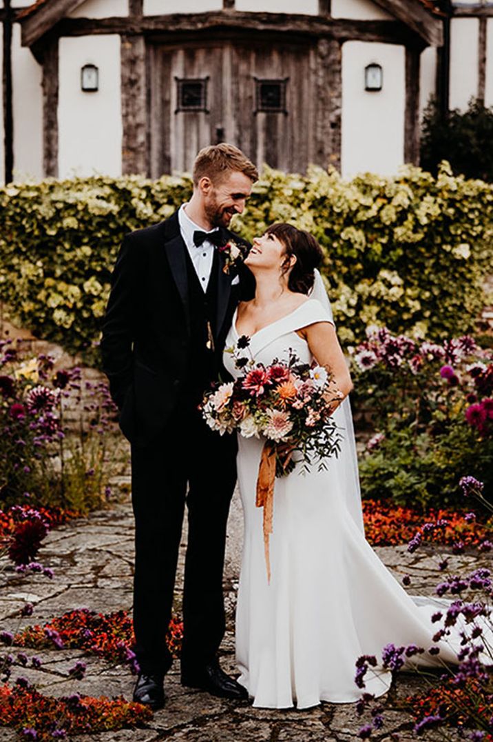 Bride in off the shoulder wedding dress with groom in black tuxedo at barn wedding venue 