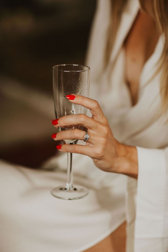 Bride with red nail polish holding a champagne glass showing off her diamond engagement ring 