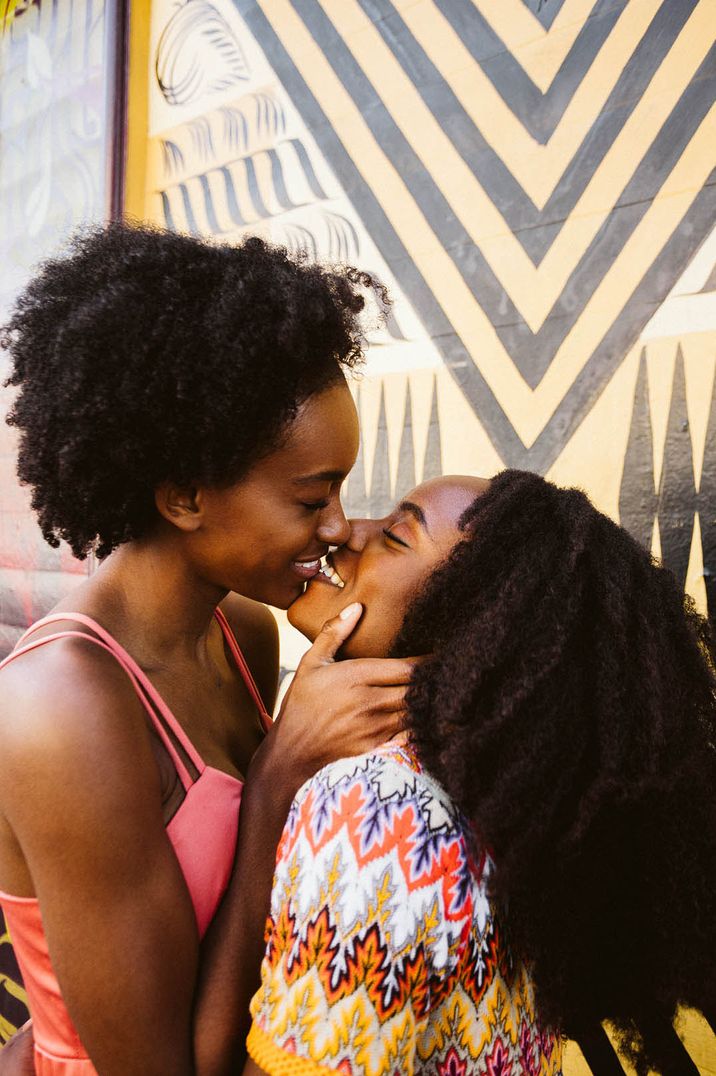 Couple share a kiss in front of colourful and patterned background 