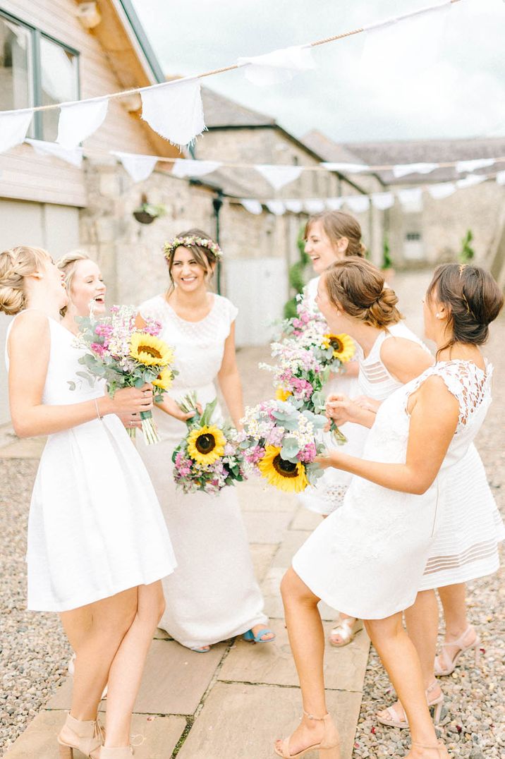 Bridesmaids wearing short white bridesmaid dresses and holding large sunflower bouquets