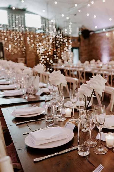 Minimalistic wedding tablescape in reception room of Shoreditch Studios London wedding venue - white rose centrepieces, fairy lights and tea light candles 