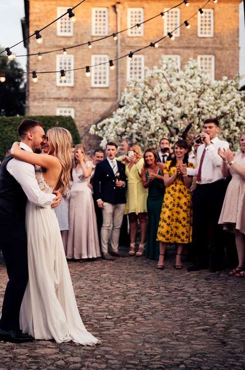 Bride and groom doing their wedding first dance under fairylights outdoors with wedding guests watching - timeline of wedding day 