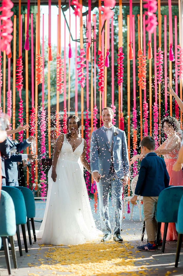 Hot pink and orange streamer wedding decor with groom in light blue suit with the bride in a lace wedding dress having confetti moment 