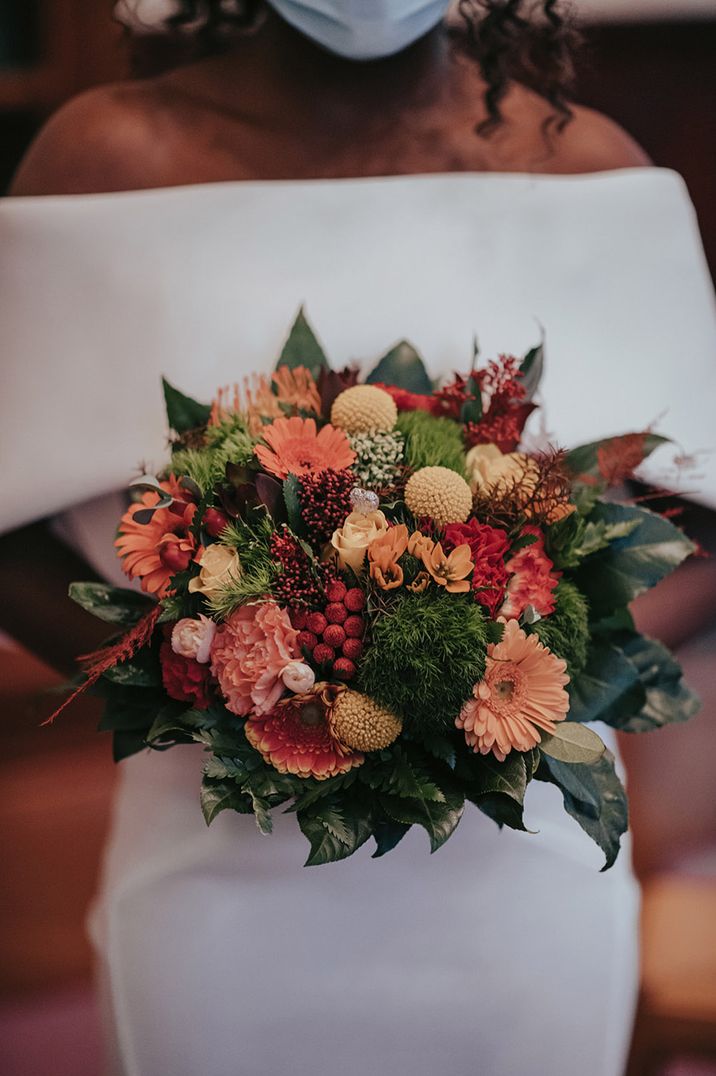 Warm toned orange, red and yellow small round wedding bouquet with greenery 