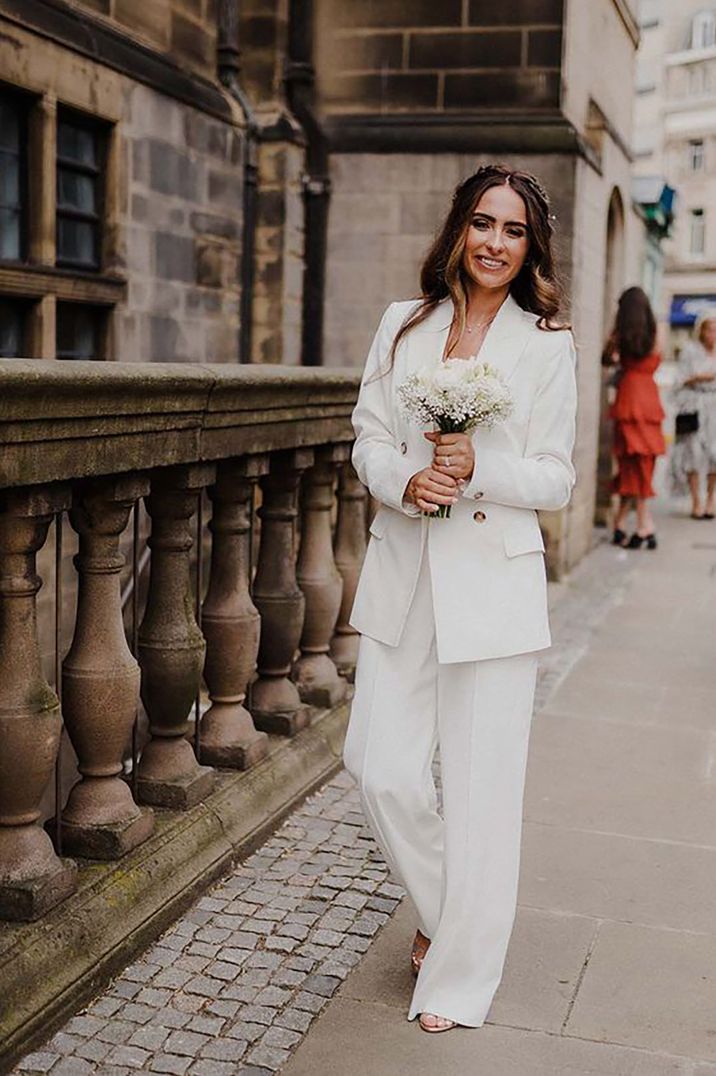 Bride in stylish bridal suit holding a white bouquet for registry office wedding