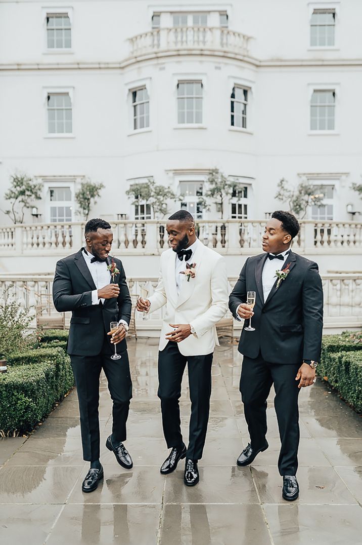 Groom and two groomsmen in tuxedos at country house wedding 