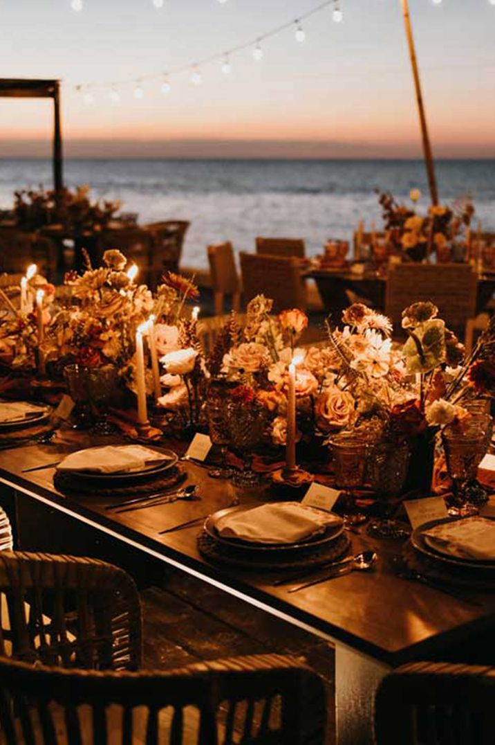 Outdoor wedding tablescape for destination wedding with cosy lighting and autumnal inspired decor with autumn leaves and dried flowers 