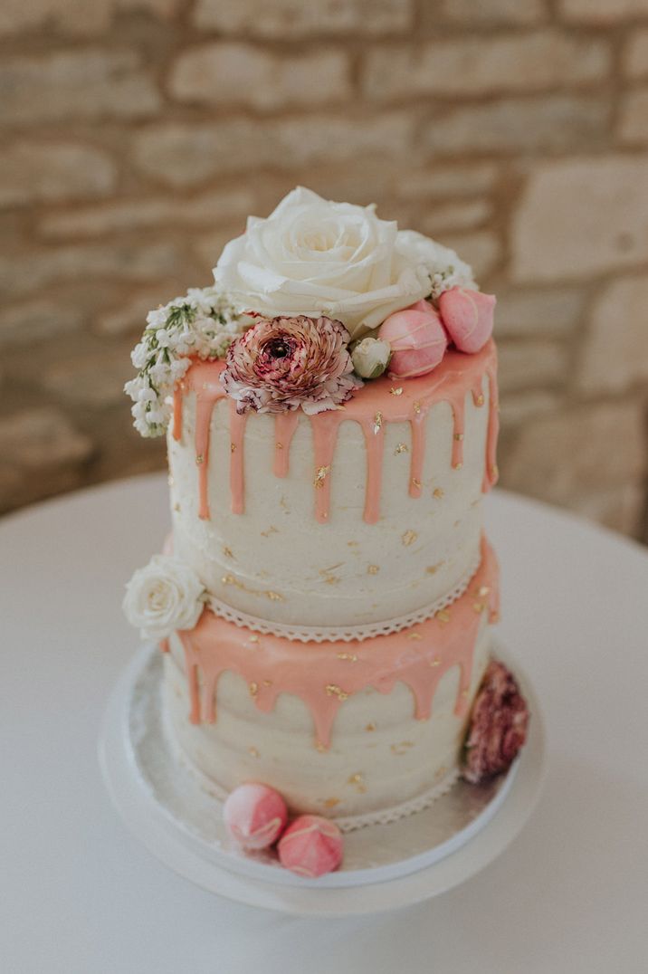 Two tier wedding cake with buttercream frosting, pink drip icing, meringue kisses and rose decor 