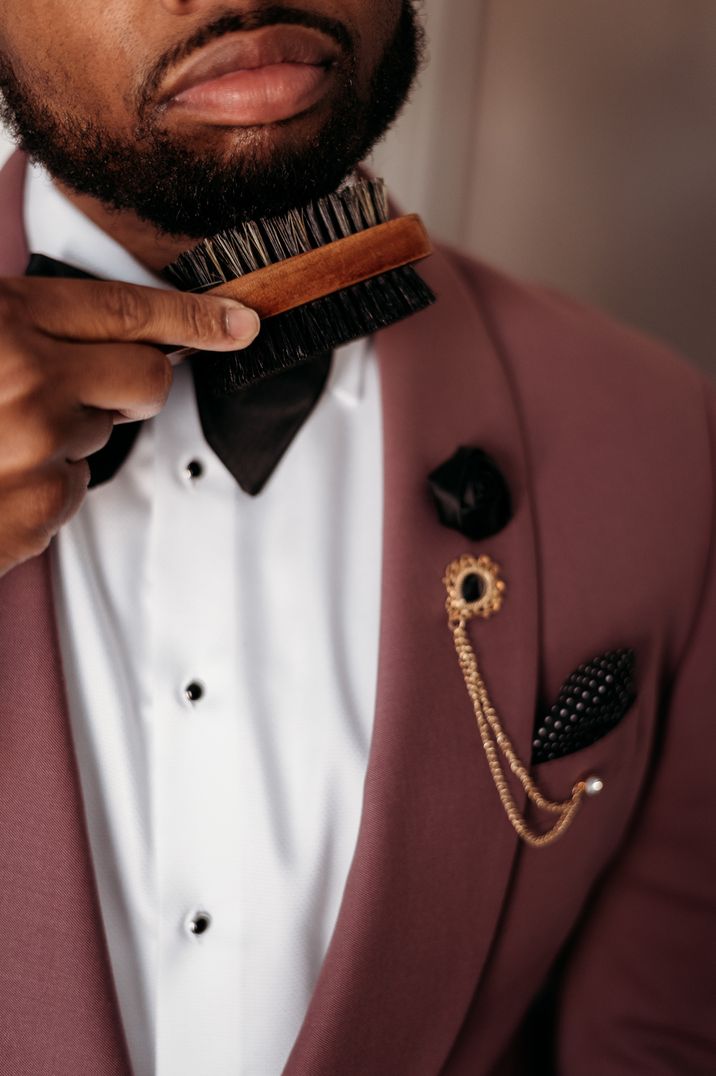 Groom in a pink suit jacket with satin rose buttonhole, black and white polka dot pocket square and gold chain accessory 