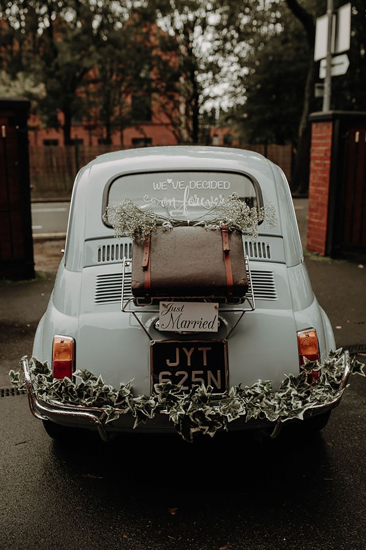 Wedding car decoration with "we've decided on forever" and "Just Married" signs, suitcase bumper and floral decorations