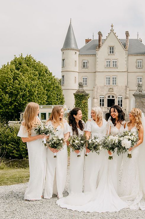 Bridal party standing outside Chateau De La Motte Husson wearing long white bridesmaid dresses