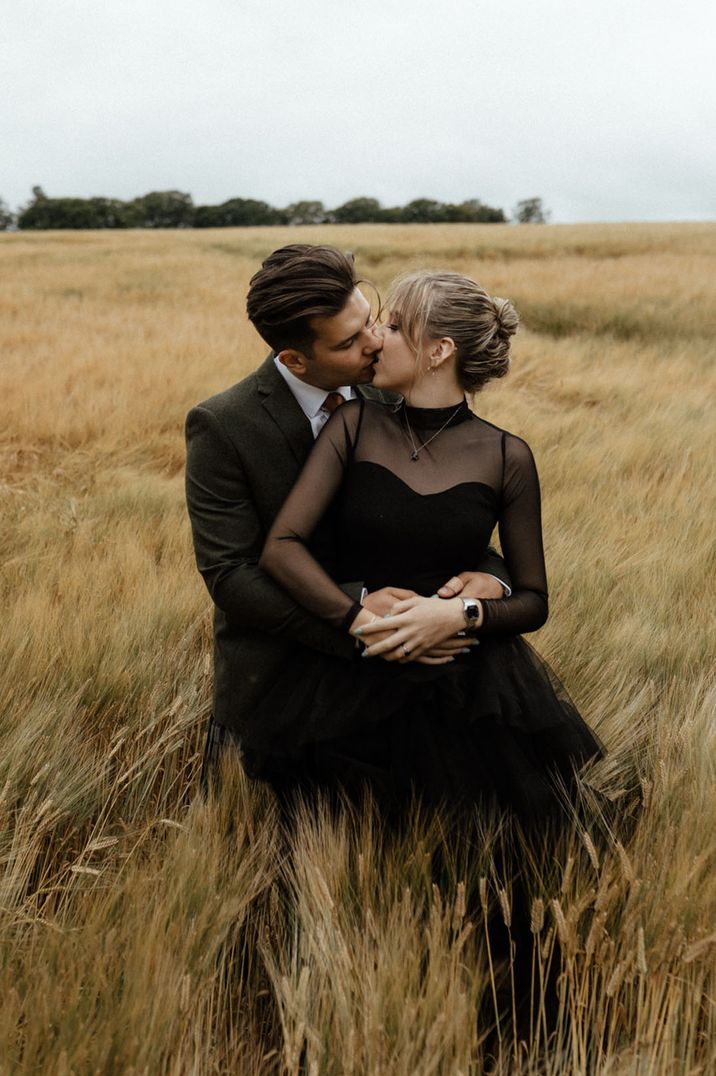 Groom in a green suit jacket embraces the bride from behind in a black wedding dress for a under 5k wedding 