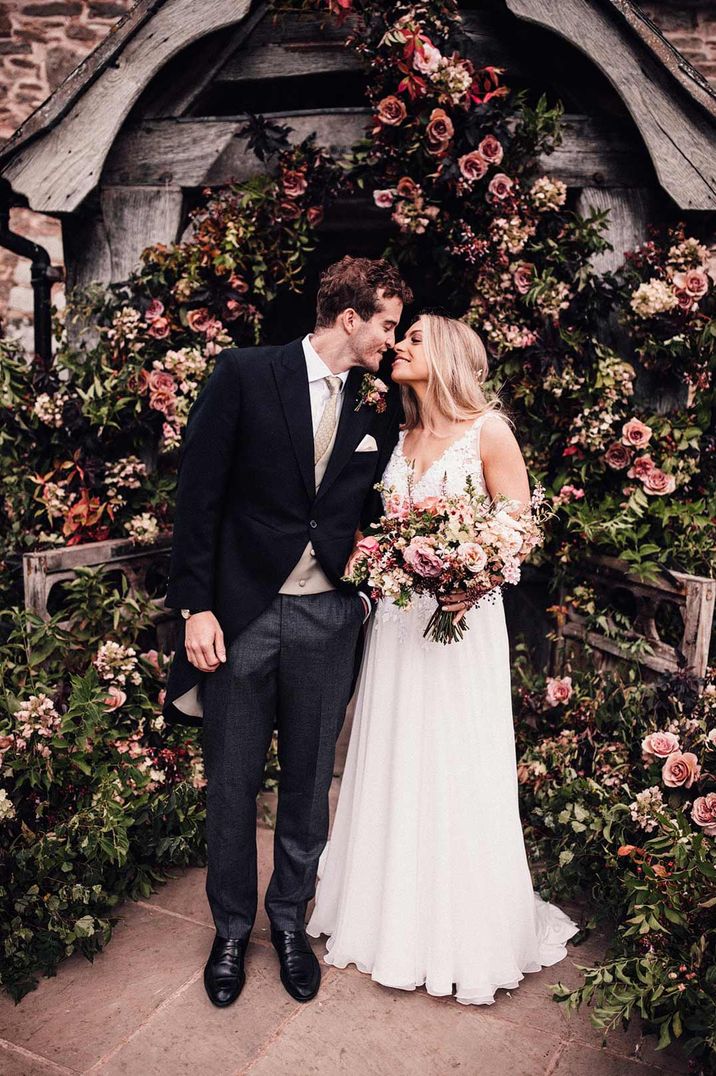 Bride and groom standing outside rose and carnation floral wedding arch