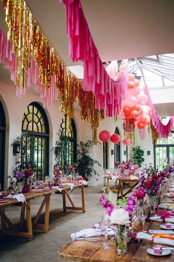 Colourful wedding reception room at Middleton Lodge Estate - gold and pink wedding streamers, pink balloons, purple floral arrangements and white napkins 