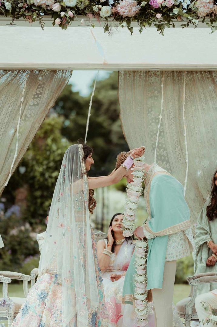 Bride and groom putting pastel coloured leis on each other at Helmingham Hall